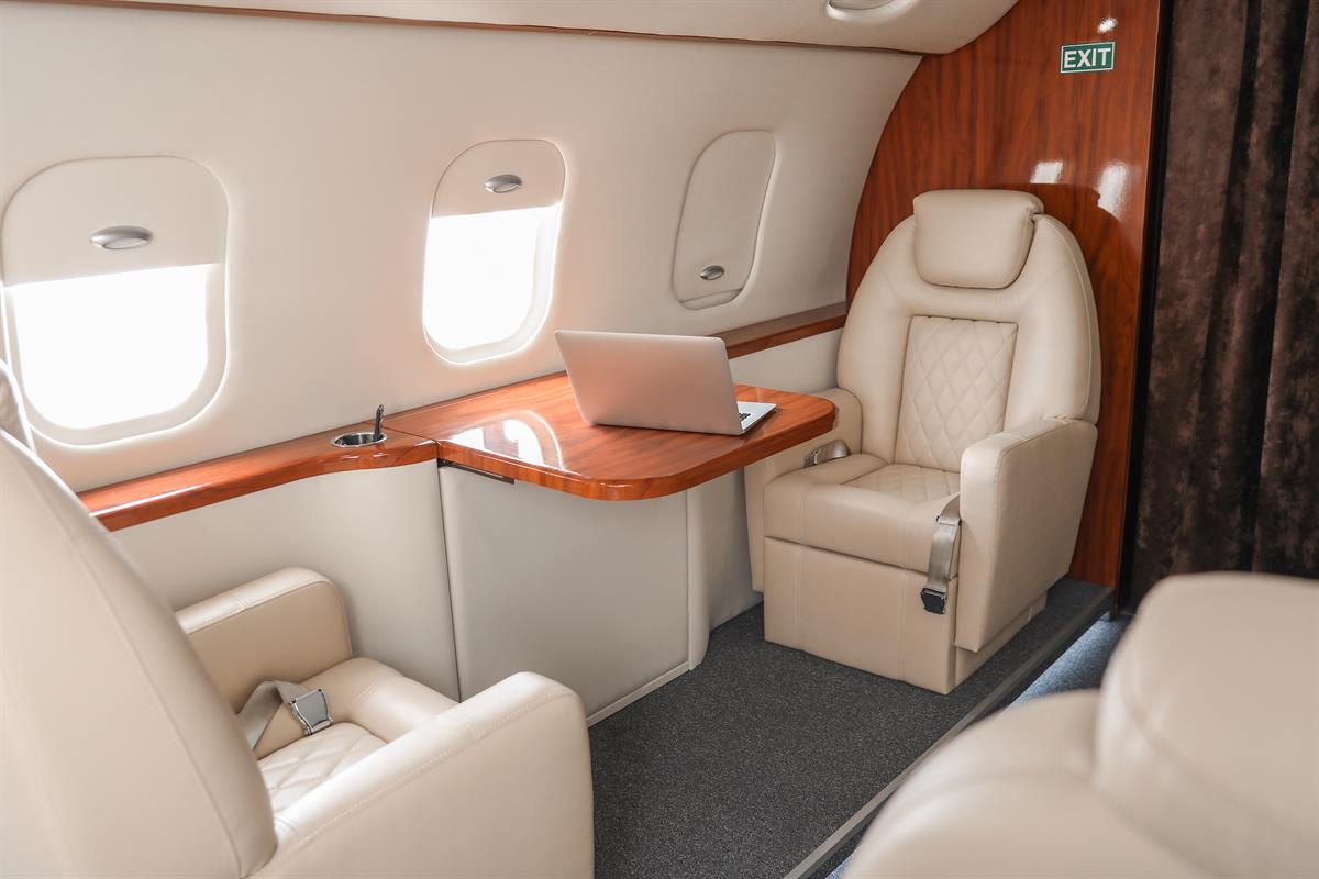 Kabine eines Privatjets mit hellen Ledersitzen, Holzverkleidung und Tisch